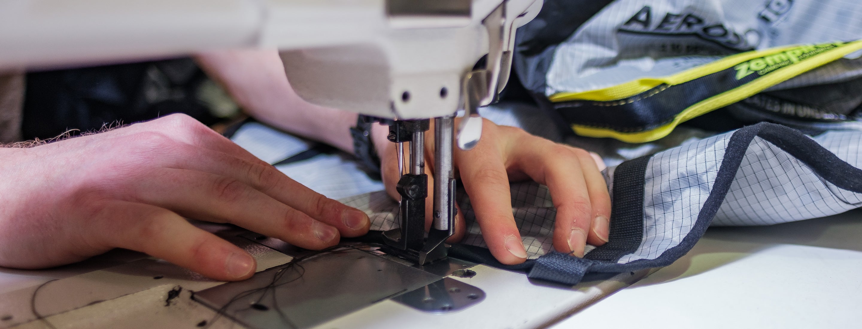 Person using a sewing machine to repair a camping bag. with fabric in the background